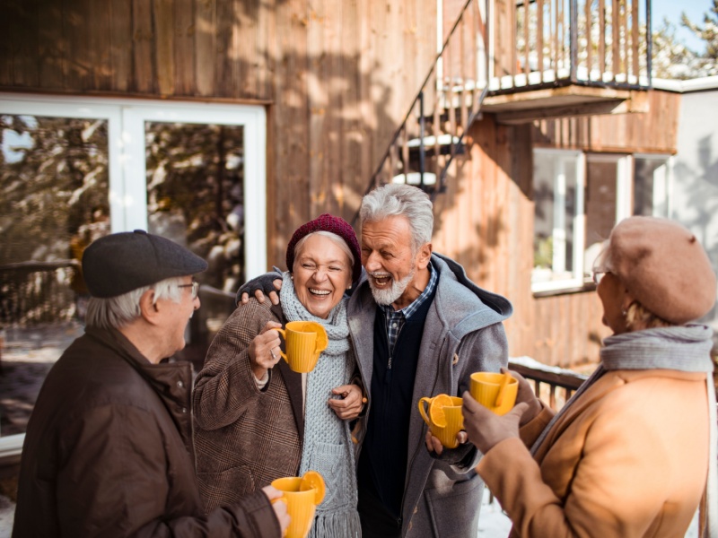 Four people with mugs standing outside laughing in winter.