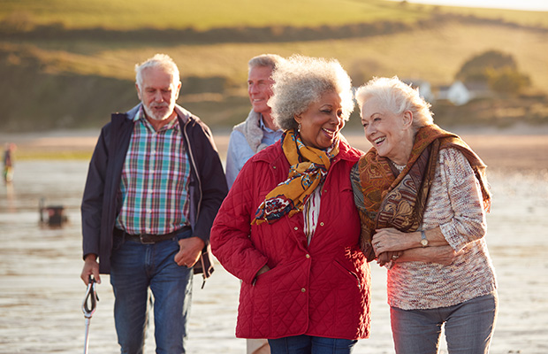 A group of people walking on the beach while chatting happily.
