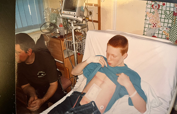 Kieran Cooper lying in a hospital bed as a teenager, showing his wound post-op