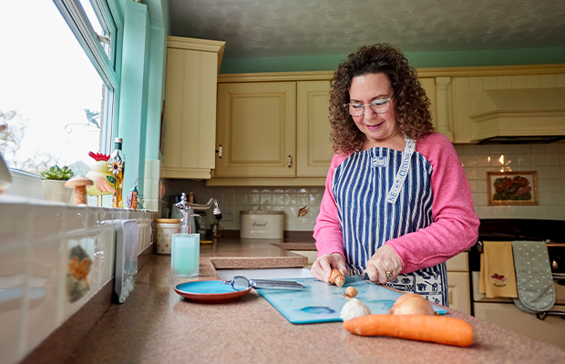 Woman wearing a striped apron chopping up vegetables on the kitchen counter