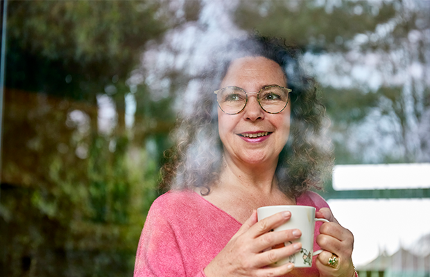 Woman wearing a pink top holding a white mug and looking out the window