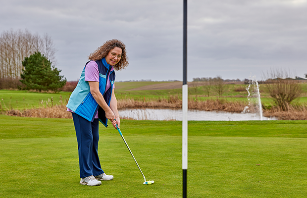 Woman in jeans, tshirt and jacket playing golf on a golf course