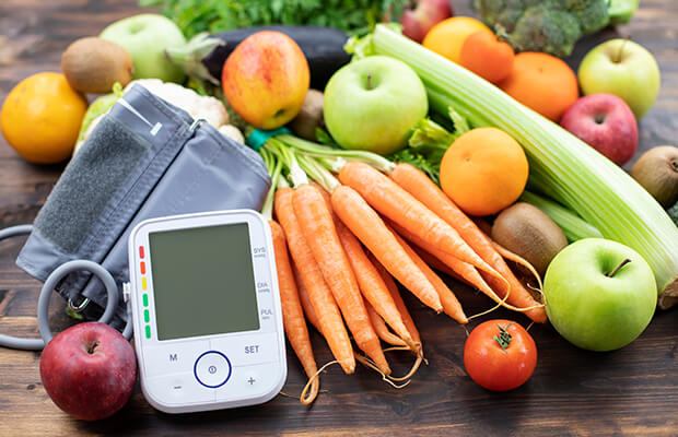 Blood pressure monitor with fresh fruit and vegetables on a wooden table