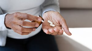 A person with a pill bottle in one hand and two white capsules in their other hand
