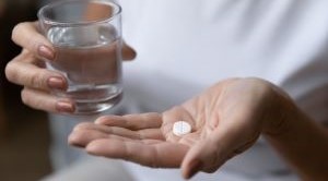Close up of a person holding an aspirin tablet and a glass of water.