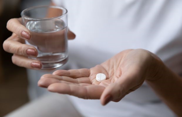 Close up of a person holding an aspirin tablet and a glass of water.