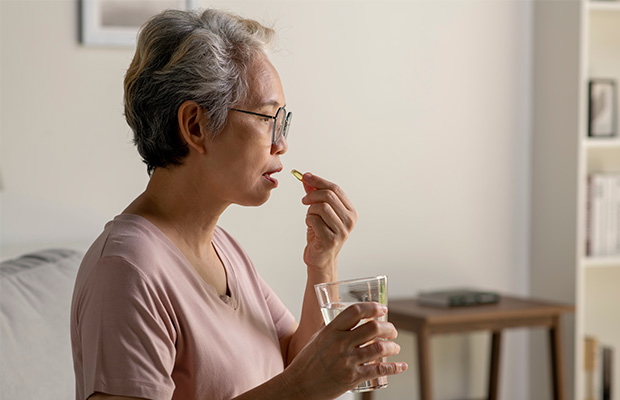 A woman takes a pill while holding a glass of water.