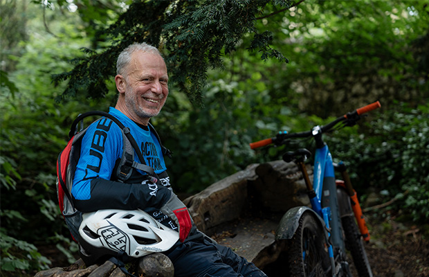 Neil Caton sitting on a log in a forest next to his electric bike.