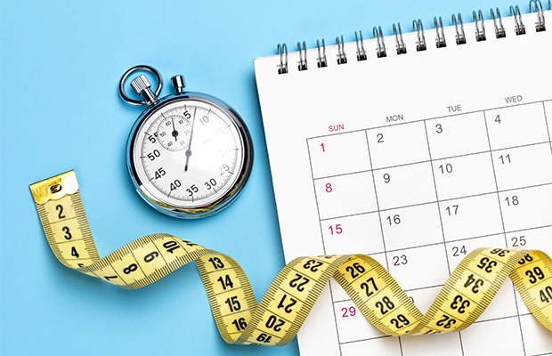 A measuring tape, calendar and stopwatch on a table.