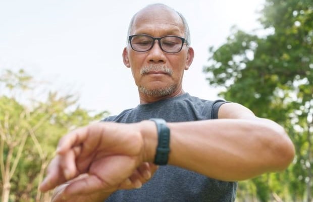 A man checks his wearable fitness tracker while exercising outside.