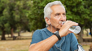 A sweaty person wearing exercise gear stops to drink water in the park.
