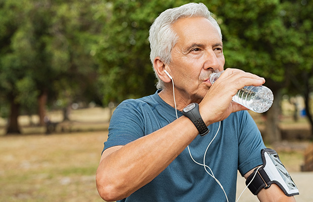 A sweaty person wearing exercise gear stops to drink water in the park.