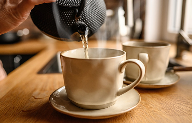 Boiling water is poured from a teapot into a mug on the kitchen counter.