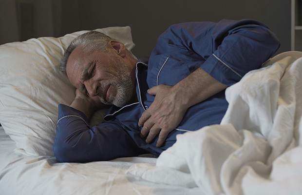 Person lying in bed at night while grimacing and holding their chest.
