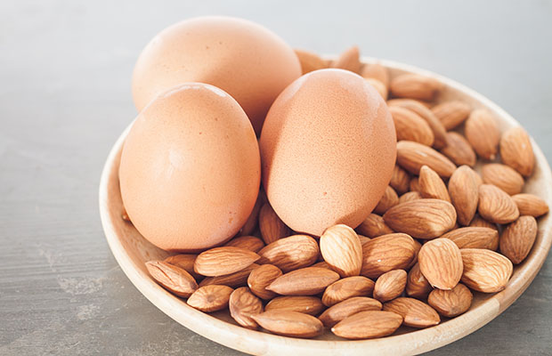 A bowl containing three eggs and a handful of almonds.