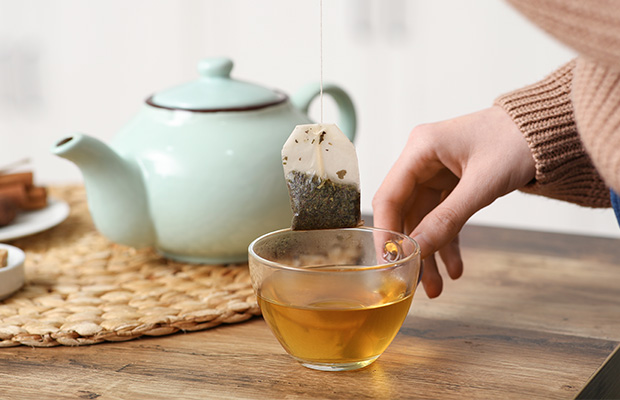 Someone takes out a teabag from a cup of green tea.