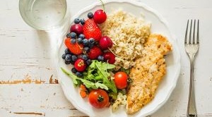 Top view of a plate of food with salad, berries, chicken and rice on.