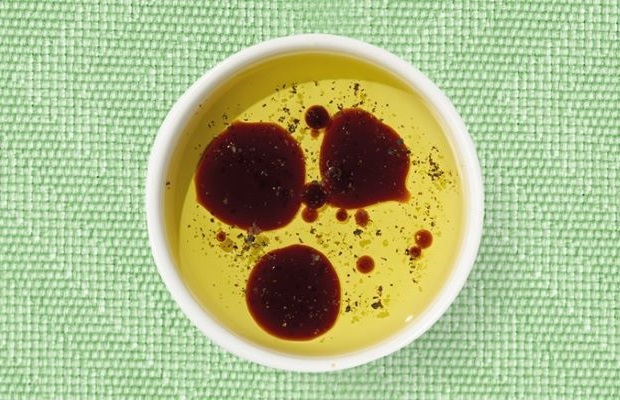 Top view of a white shallow dish containing balsamic vinaigrette, on a green tablecloth.