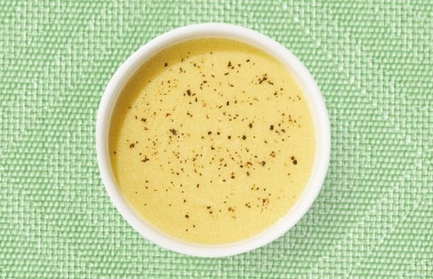 Top view of a white shallow dish containing French dressing, on a green tablecloth.