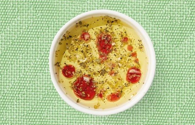 Top view of a white shallow dish containing Greek salad dressing, on a green tablecloth.