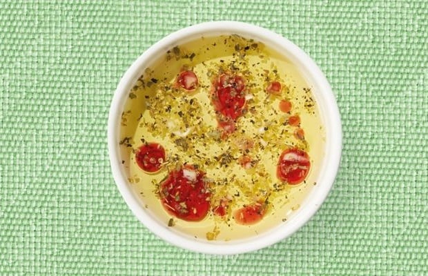 Top view of a white shallow dish containing Greek salad dressing, on a green tablecloth.