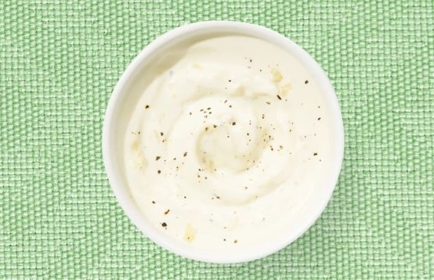 Top view of a white shallow dish containing a creamy, healthy Caesar dressing on a green tablecloth.