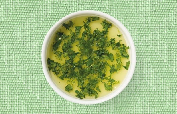 Top view of a white shallow dish containing a herb dressing, on a green tablecloth.