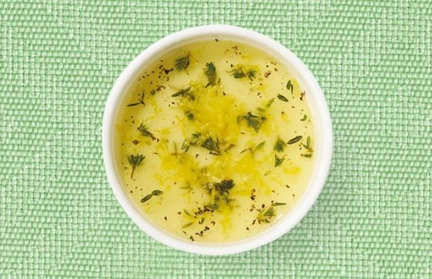 Top view of a white shallow dish with a lemon, olive oil and herb dressing on a green tablecloth.