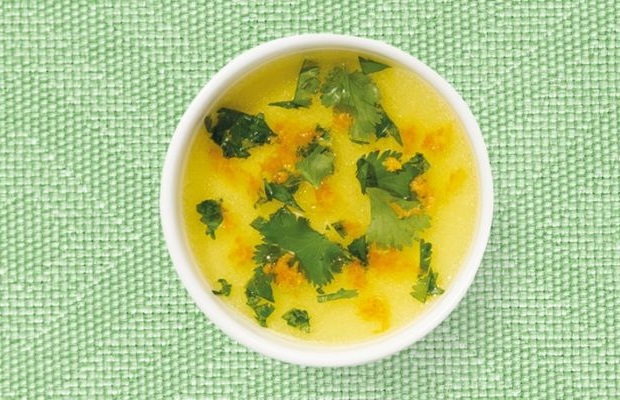 A shallow white bowl containing an orange vinaigrette, on a green tablecloth.