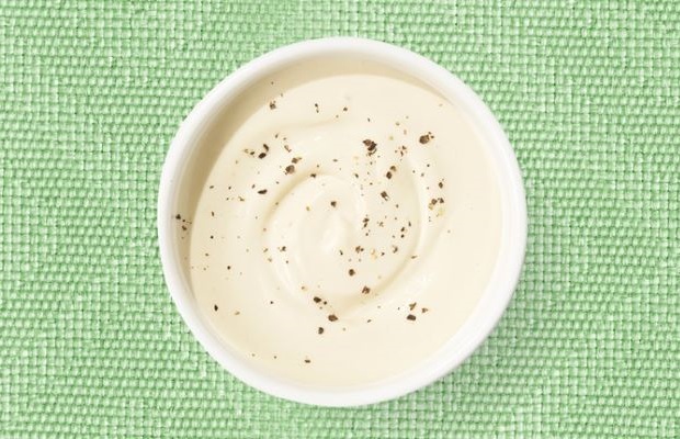 Top view of a white shallow dish containing tahini dressing, on a green tablecloth.