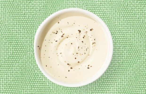 Top view of a white shallow dish containing tahini dressing, on a green tablecloth.