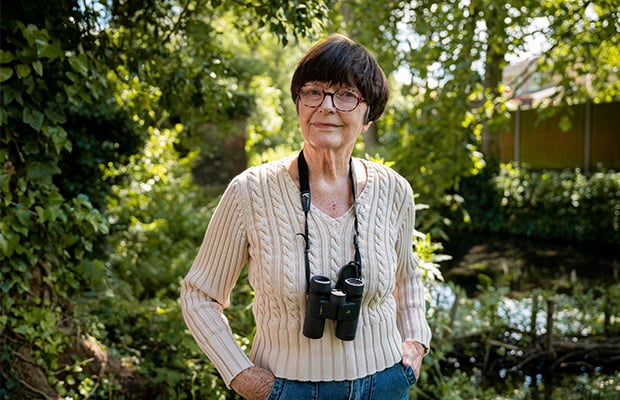 Dot standing in her garden with binoculars around her neck