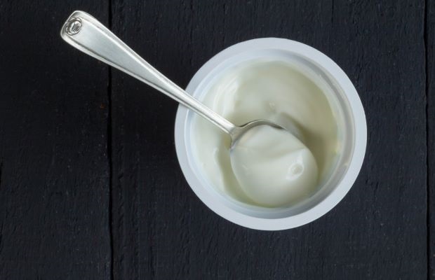 Top view of a pot of Greek yogurt with a table spoon in it.