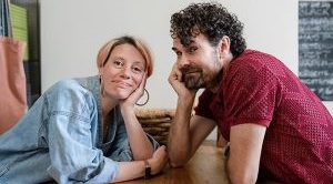 Becky and Paul sit opposite each other at a table at home.