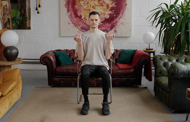 Jack Heseltine demonstrates seated biceps curls holding food cans for weights