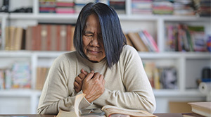 A woman puts her hands to her chest in pain