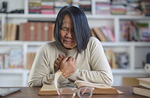 A woman puts her hands to her chest in pain