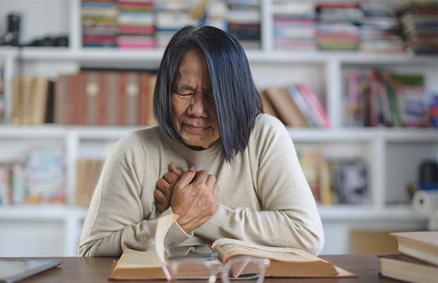 A woman puts her hands to her chest in pain