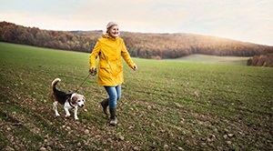 A woman walking a dog over some fields.