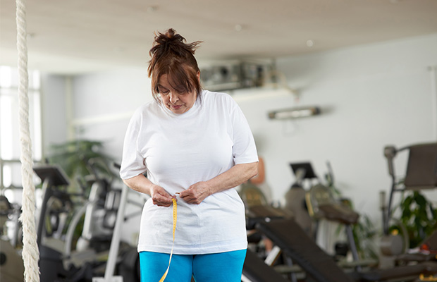 A woman measures her waist with a tape measure in a gym