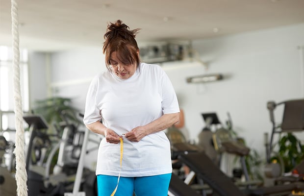A woman measures her waist with a tape measure in a gym