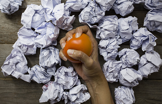 A hand squeezing a stress ball surrounded by crumpled paper