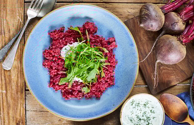 wooden table with beetroot, knife and fork and a plate of beetroot barley risotto