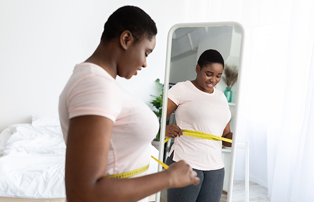 A woman at home wraps a tape measure around her waist