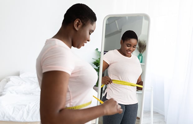 A woman at home wraps a tape measure around her waist