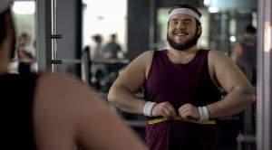 A man in a gym wraps a tape measure around his waist
