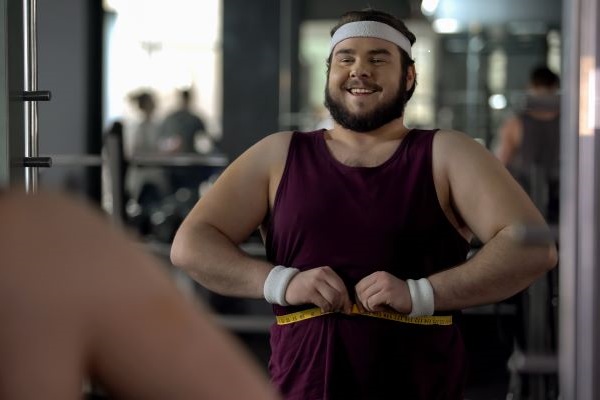 A man in a gym wraps a tape measure around his waist