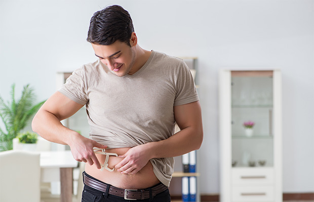 A man uses skinfold calipers to measure fat around his waist