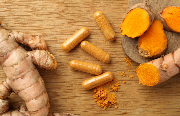 Turmeric supplements next to turmeric roots on a wooden table