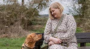 Gini Dellow sitting on a bench outside looking at her dog